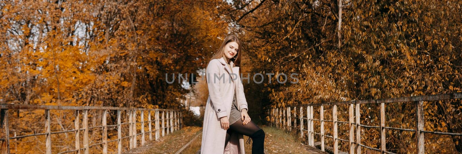 A beautiful long-haired woman walks through the autumn streets. Railway, autumn leaves, a woman in a light coat.