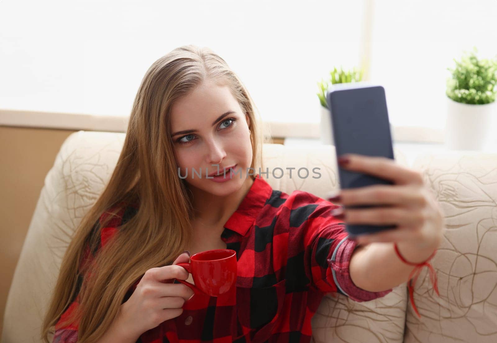 young blond pretty woman drinking coffe and look at laptop in morning sit on sofa