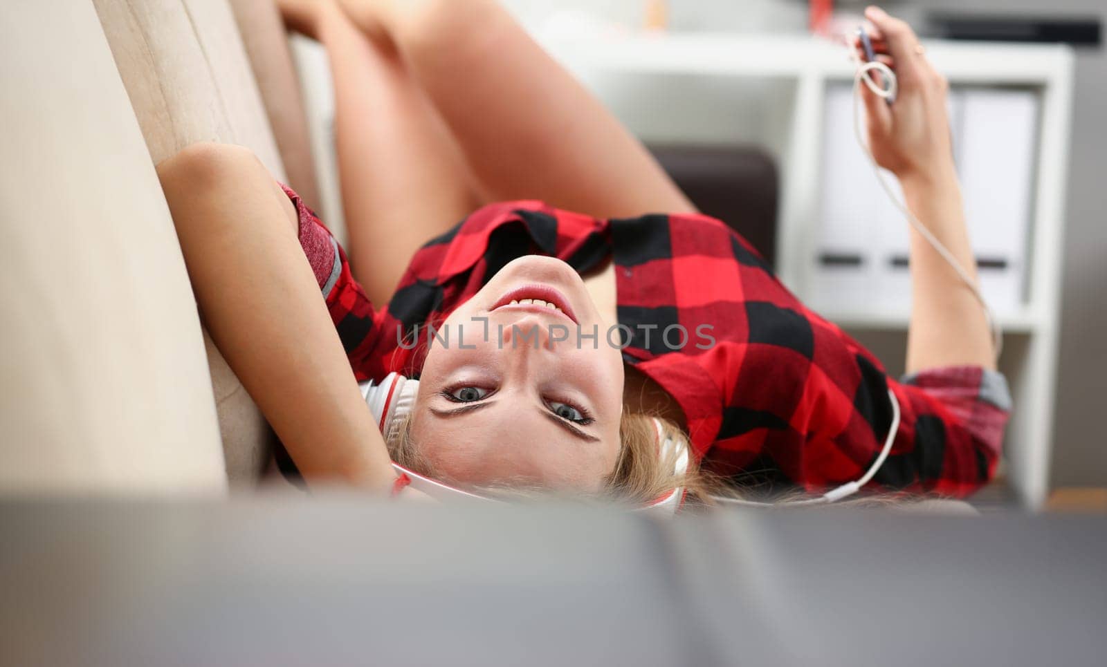 blond young pretty woman listen music lie on sofa hold laptop in arms