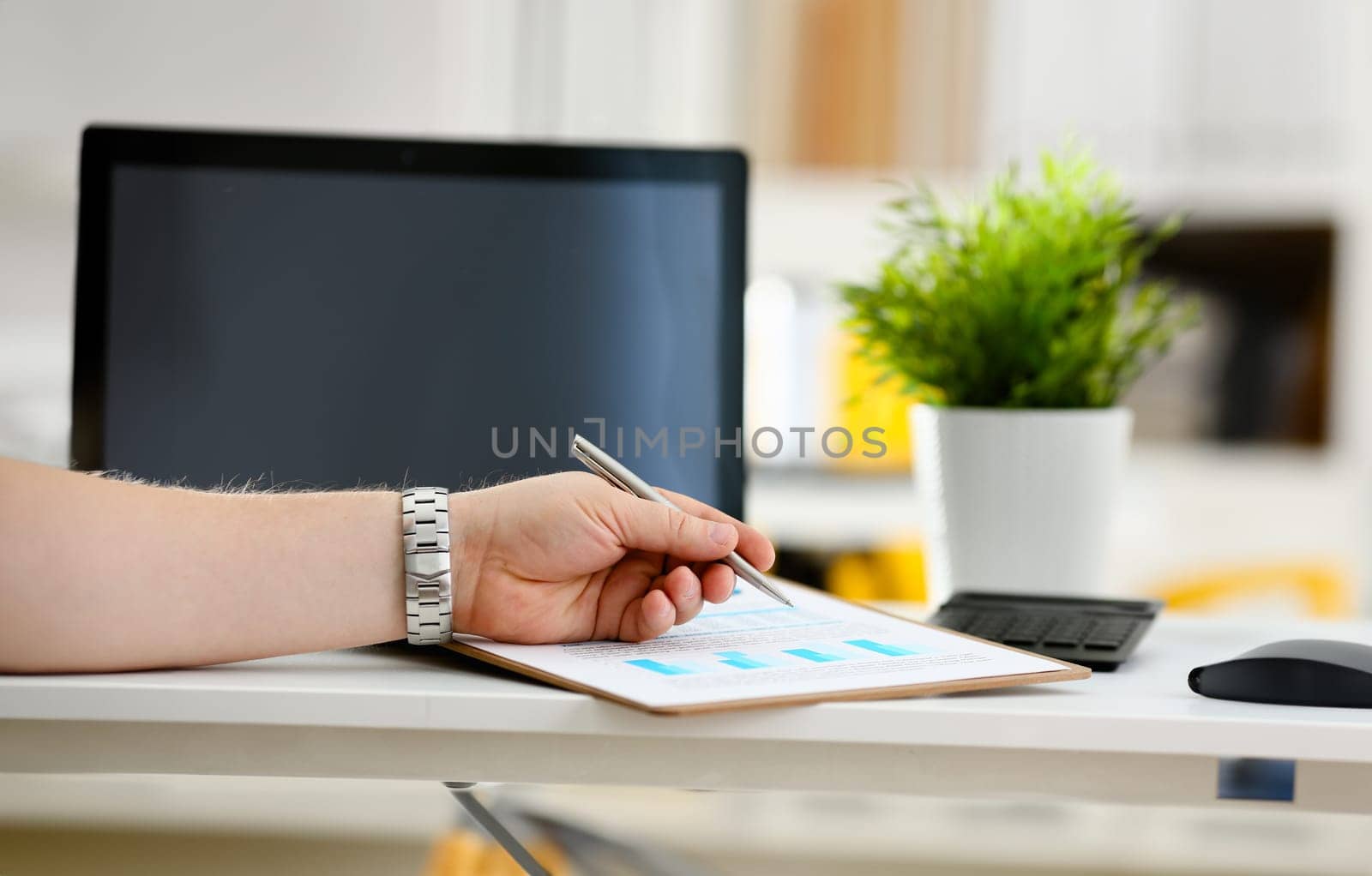 Male arm hold silver pen examining stats graphic clipped to pad in office closeup. Stock exchange market advisor participate in negotiation study trade process inspector check or explain money data