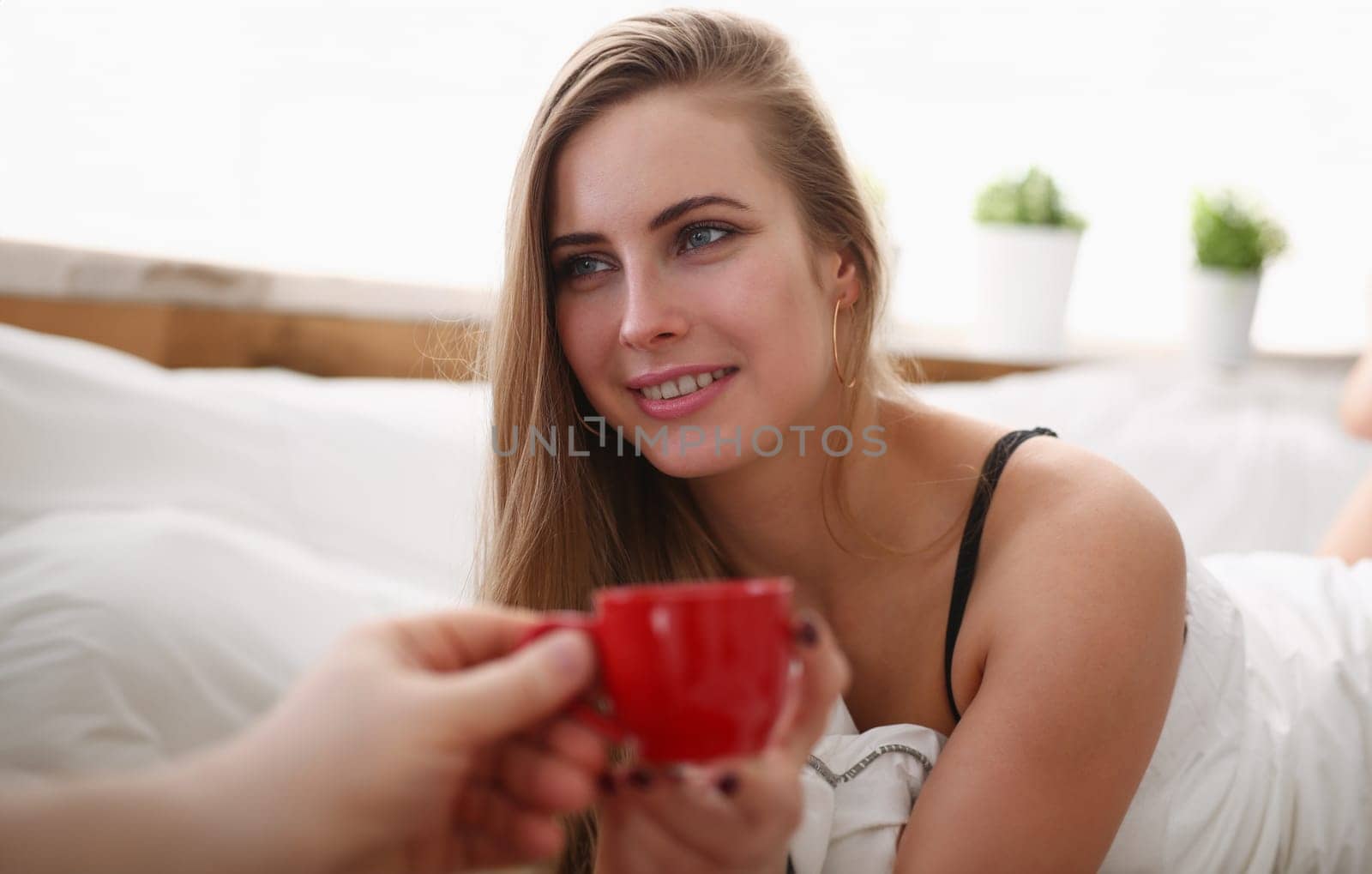young pretty blond woman have cup of tea coffee early morning in her bed