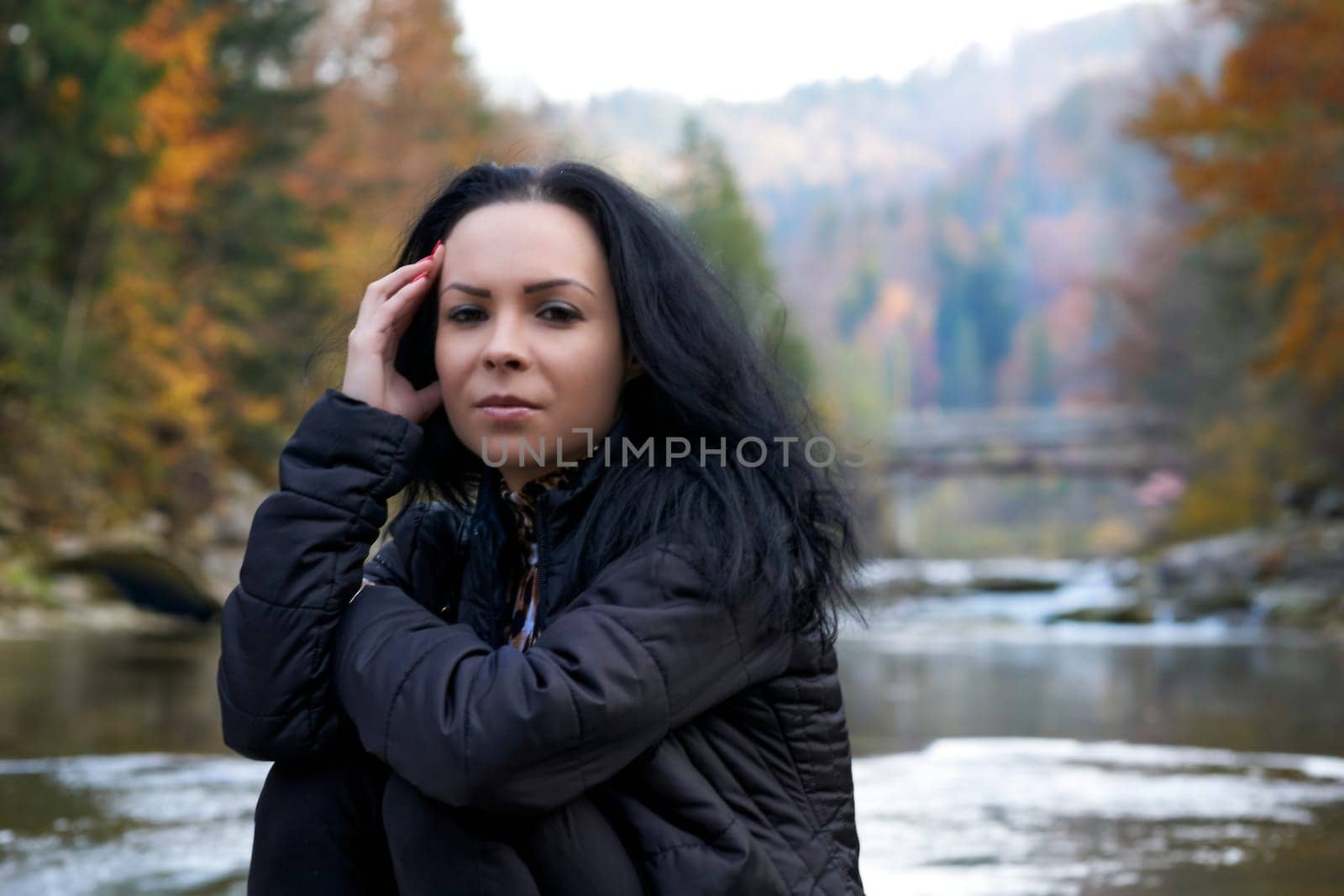 Serious young brunette woman on the bank of an autumn mountain river by jovani68
