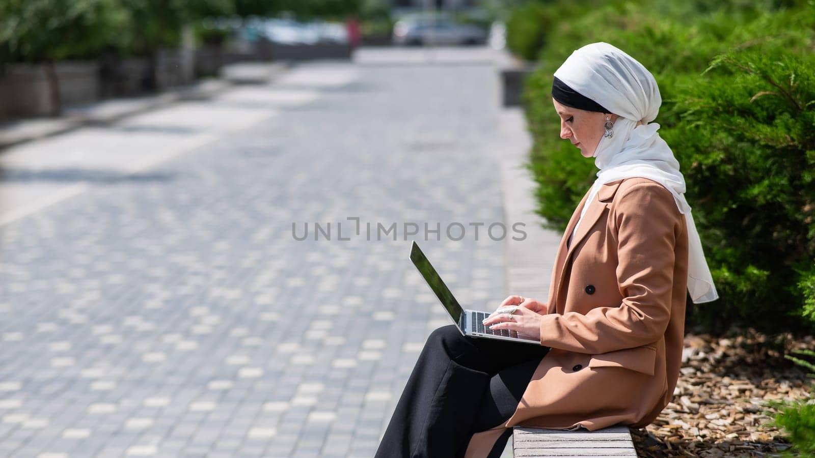 Portrait of young woman in hijab using laptop outdoors. by mrwed54