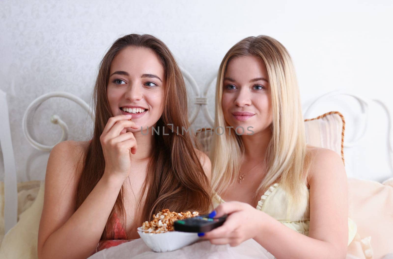 Two happy smiling girlfriends eat popcorn in bed by kuprevich