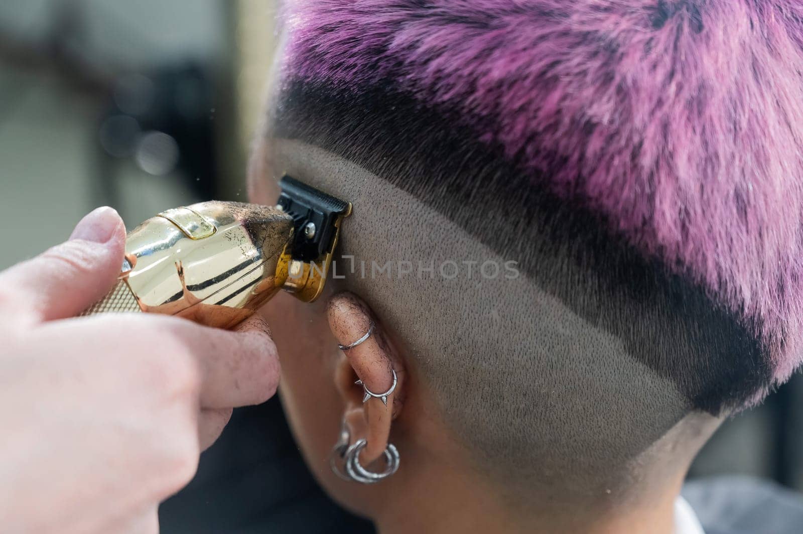 The hairdresser shaves the temple of a female client. Rear view of a woman with short pink hair in a barbershop