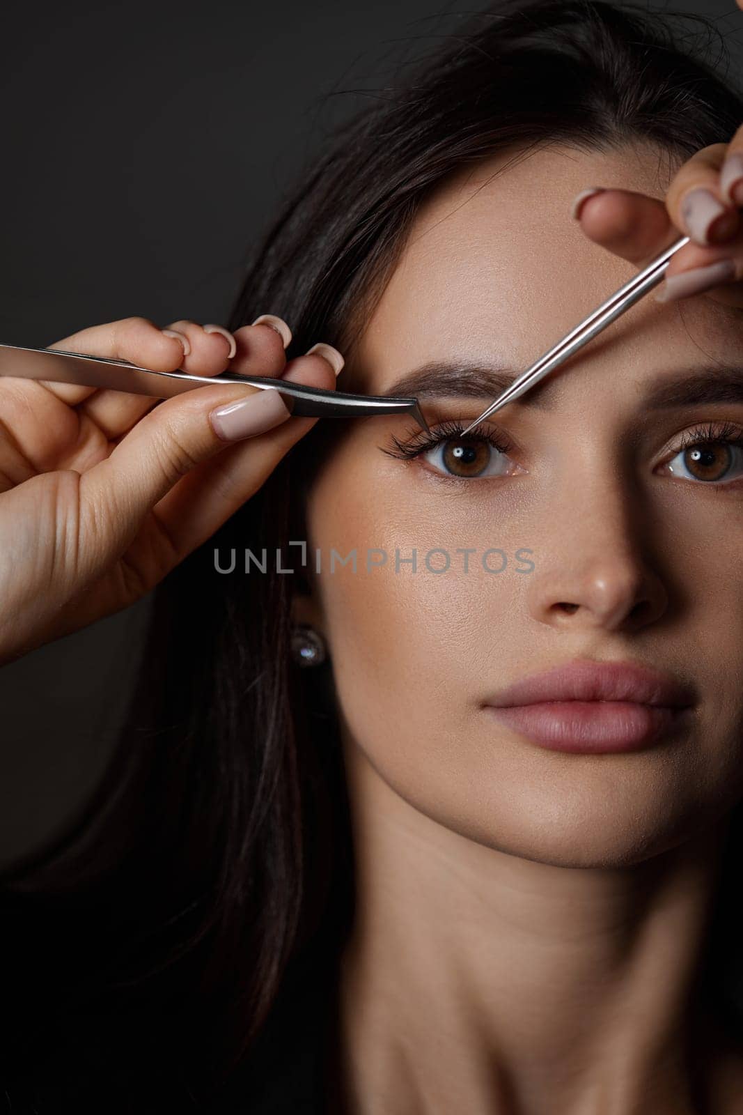 beauty professional woman holding eyelash tweezers while posing on black background. close-up