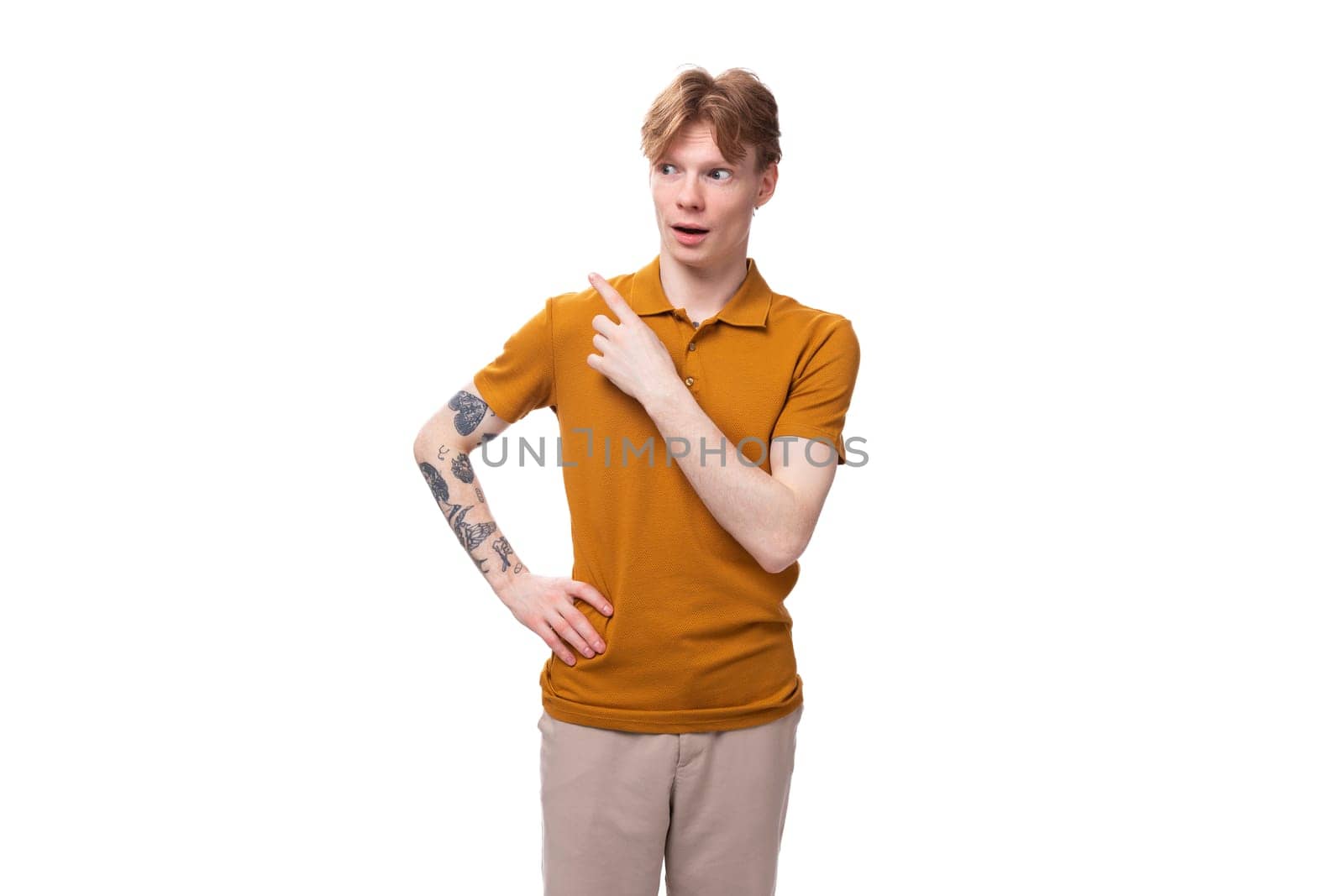 young red-haired caucasian student man with a tattoo dressed in a mustard t-shirt gesturing.