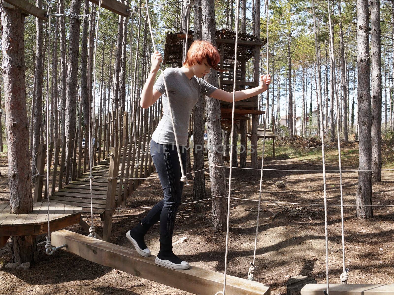 teenage girl walking on a suspended log in a rope training camp.