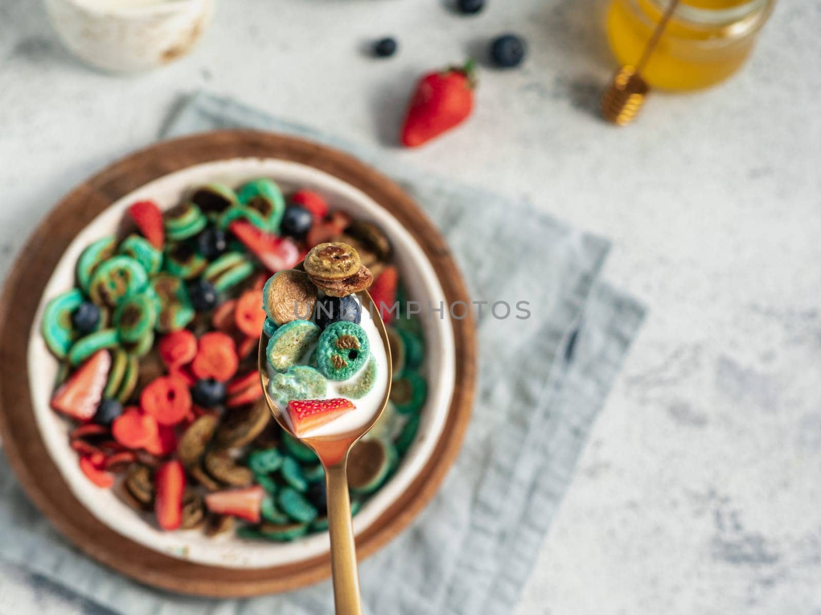 Trendy food - pancake cereal. Bowl of colorful mini cereal pancakes in spoon with milk. Tiny pancakes with natural color - green matcha, turquose spirulina, blue pea, red fragon fruit. Copy space