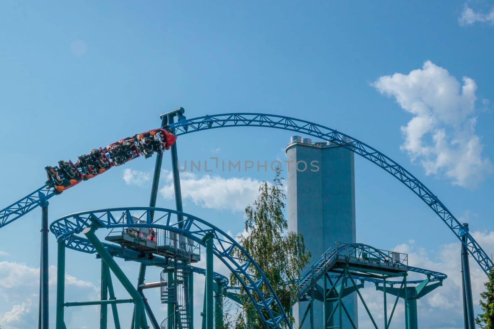 Helsinki, Finland - 19 AUGUST 2024: Linnanmaki amusement park with roller coaster Taiga in motion, blue sky on a background, happy people