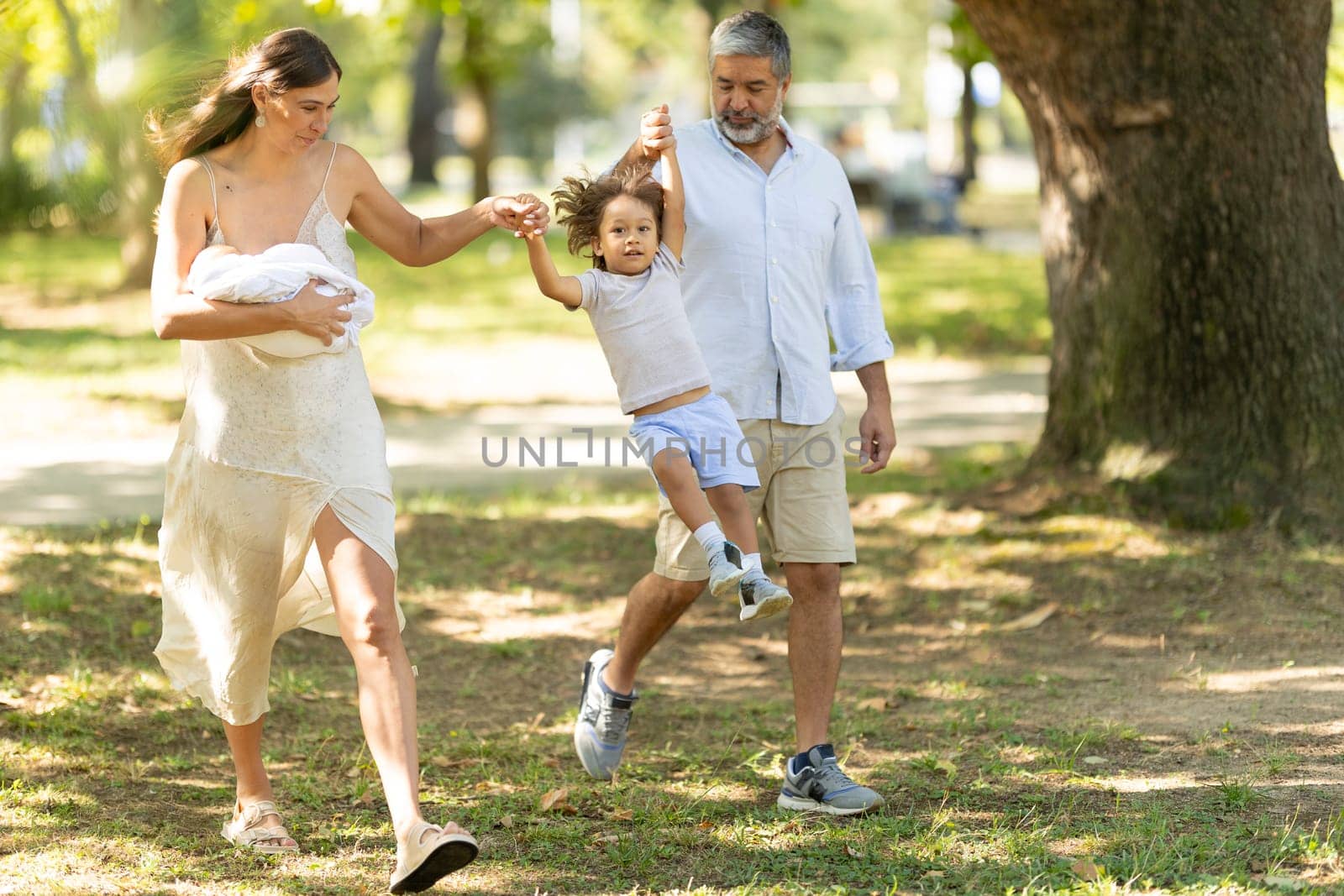 Family is enjoying a walk in the park, with the father lifting their son in the air