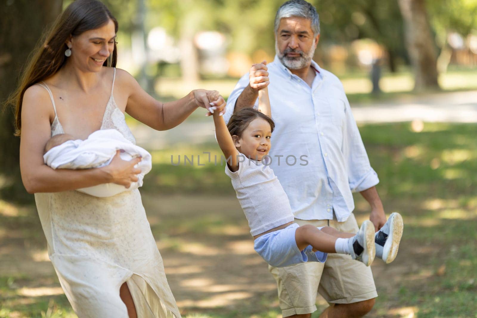 Happy family is enjoying a sunny day at the park, swinging their son between them as they walk
