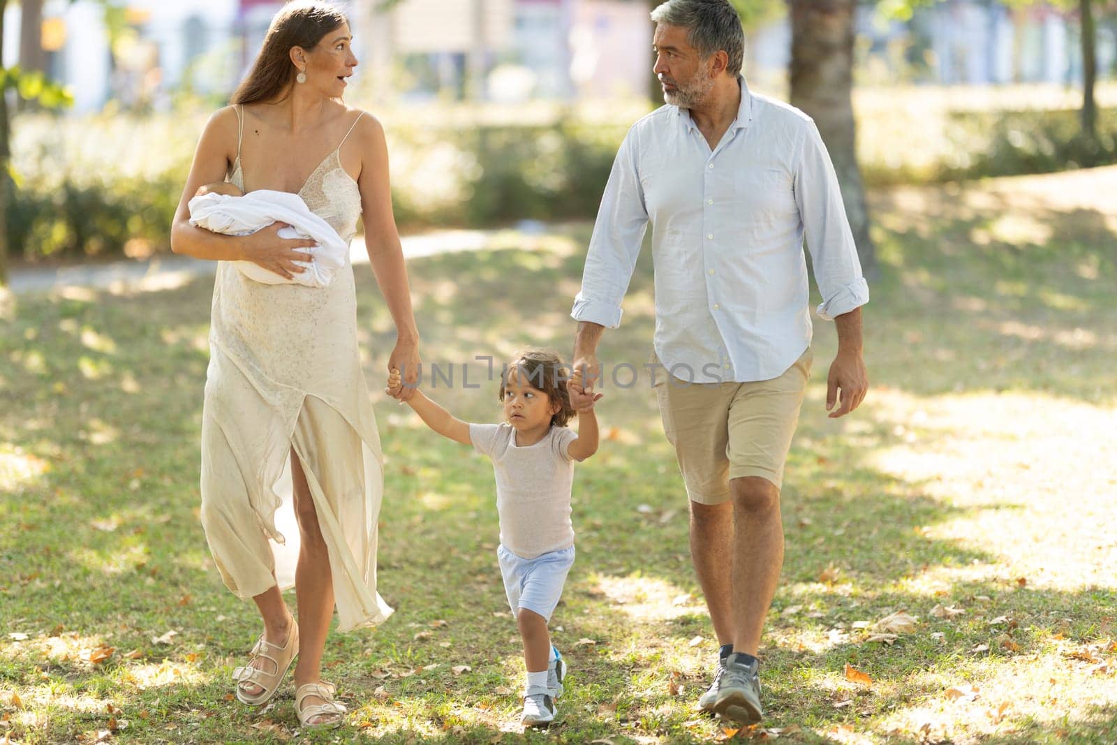 Young family is enjoying a sunny day out at the park, holding hands and walking together