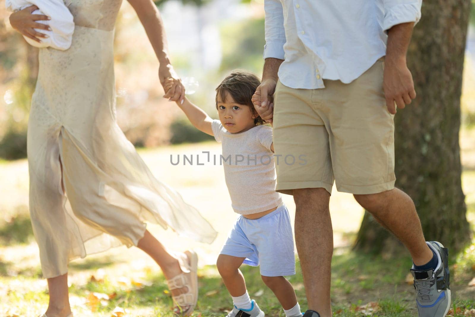 Young family enjoys a sunny day out, taking a leisurely stroll through the park with their two children