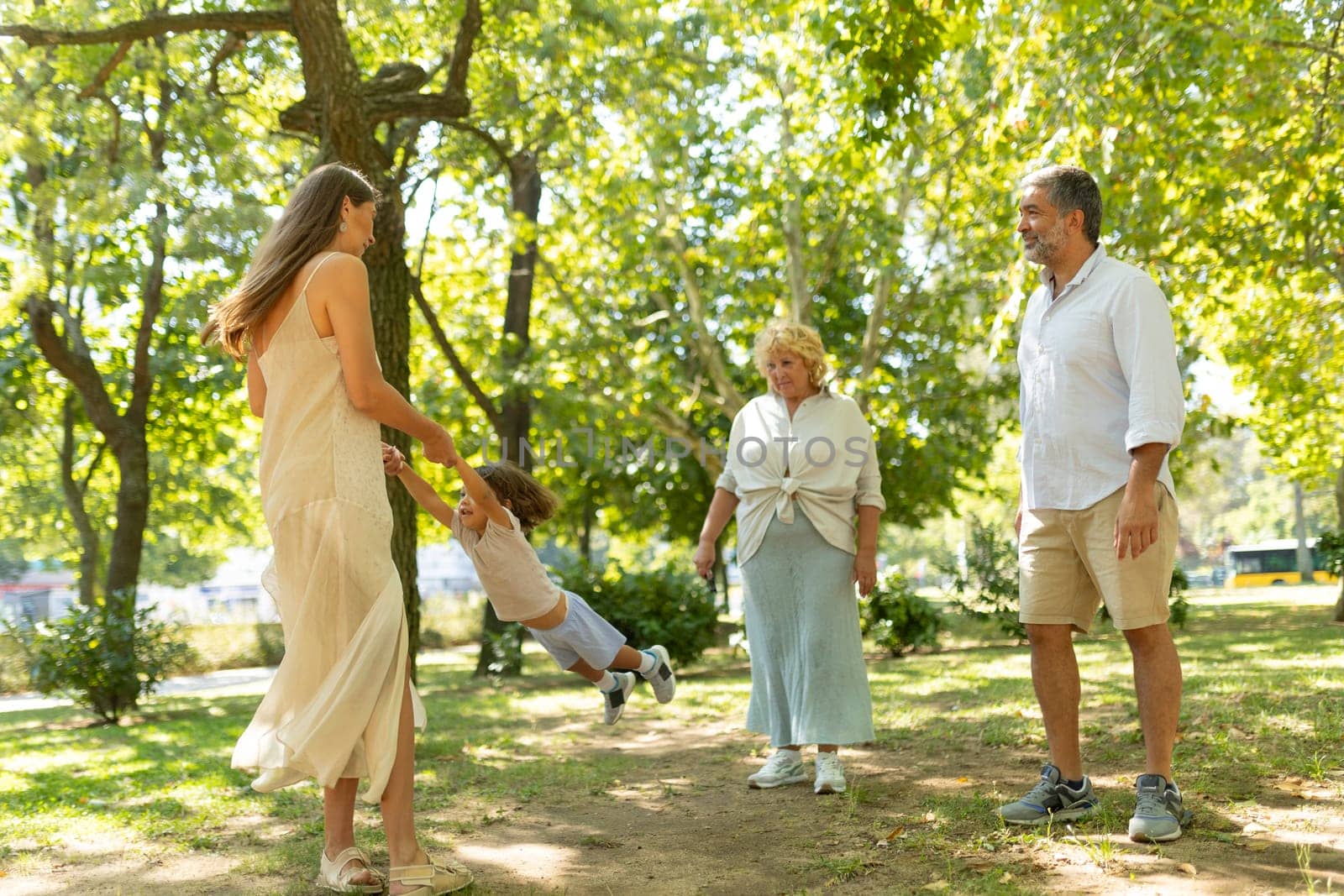 Cheerful multigenerational family enjoying a sunny day in the park, with a mother swinging her child