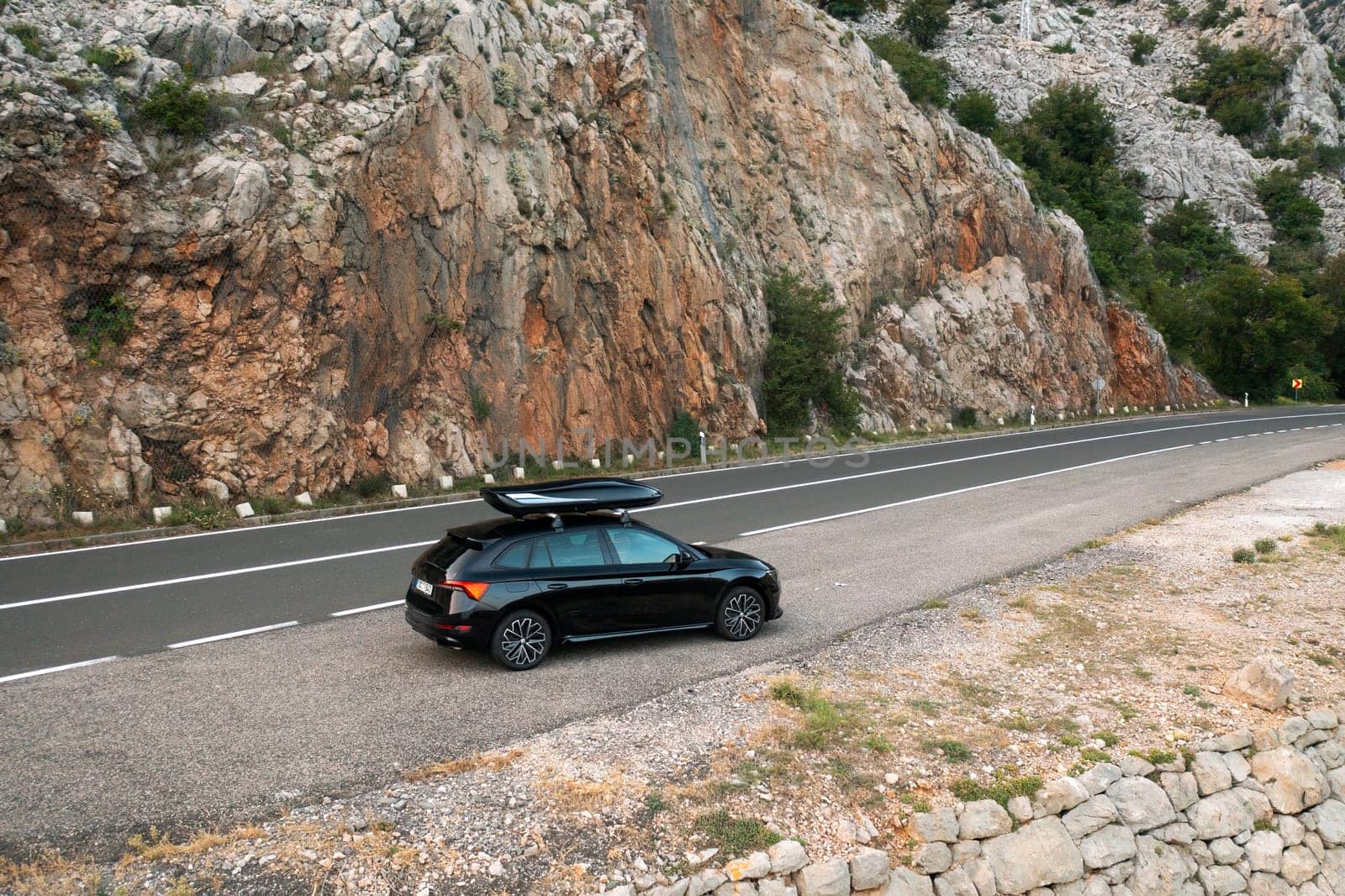 A black car parked near a rocky landscape along a winding mountain road.