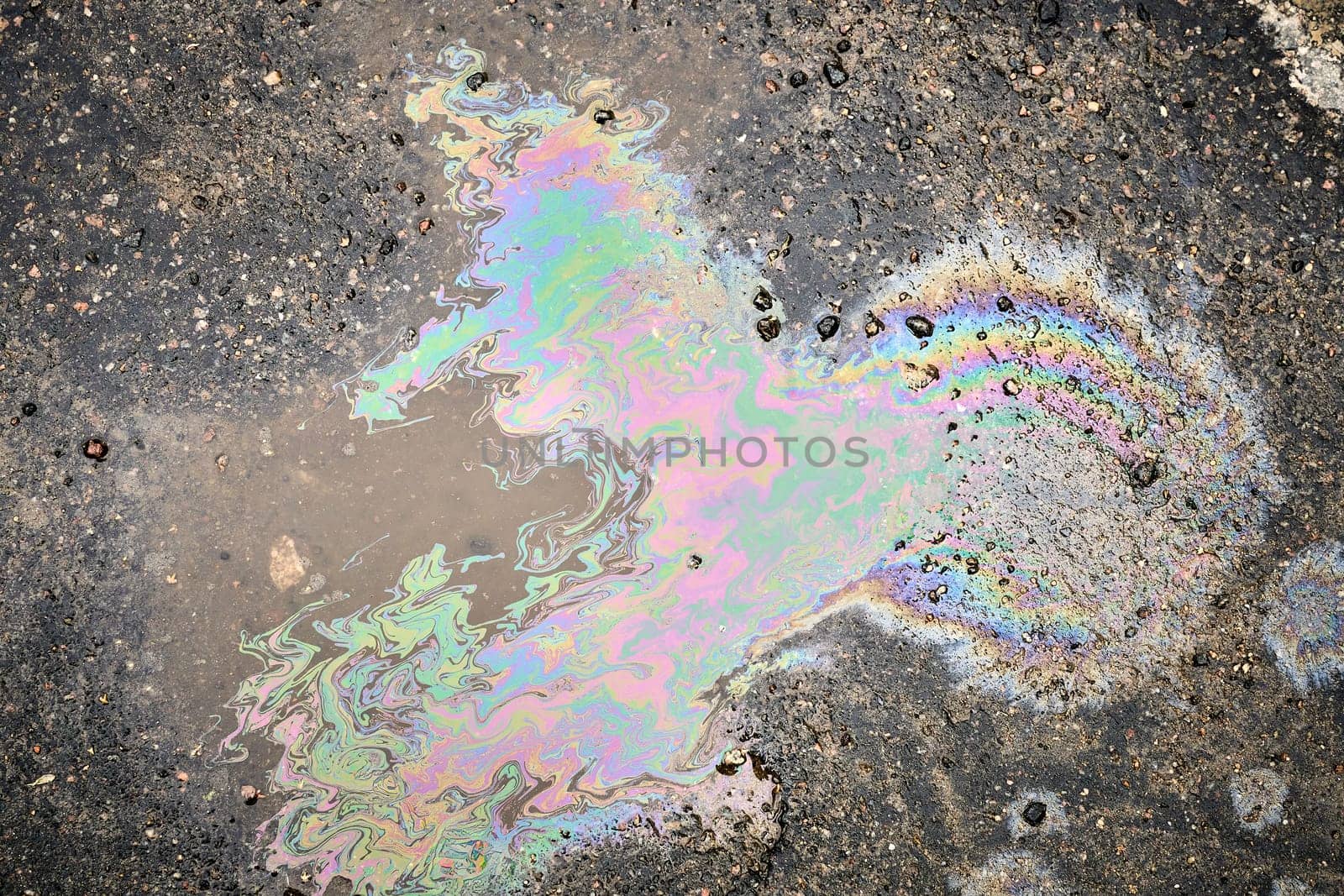 A close-up of a shimmering oil or fuel spill on wet asphalt, viewed from above.
