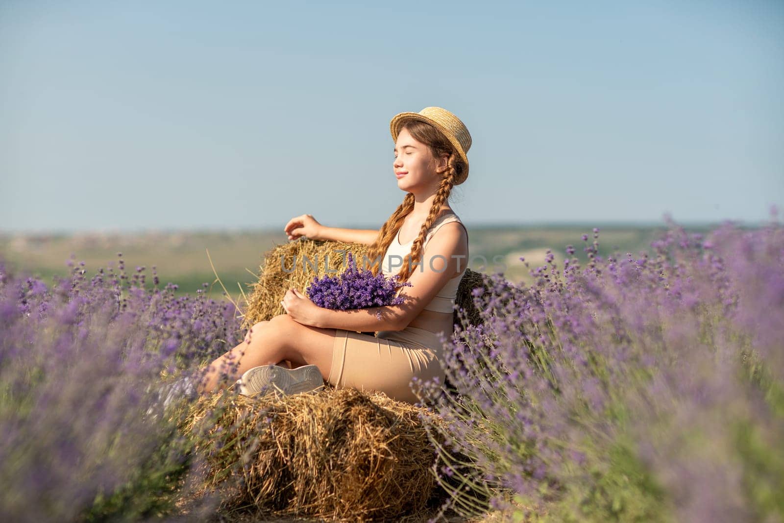girl sitting field lavender and wearing a straw hat. She is smiling and holding a bouquet of flowers.