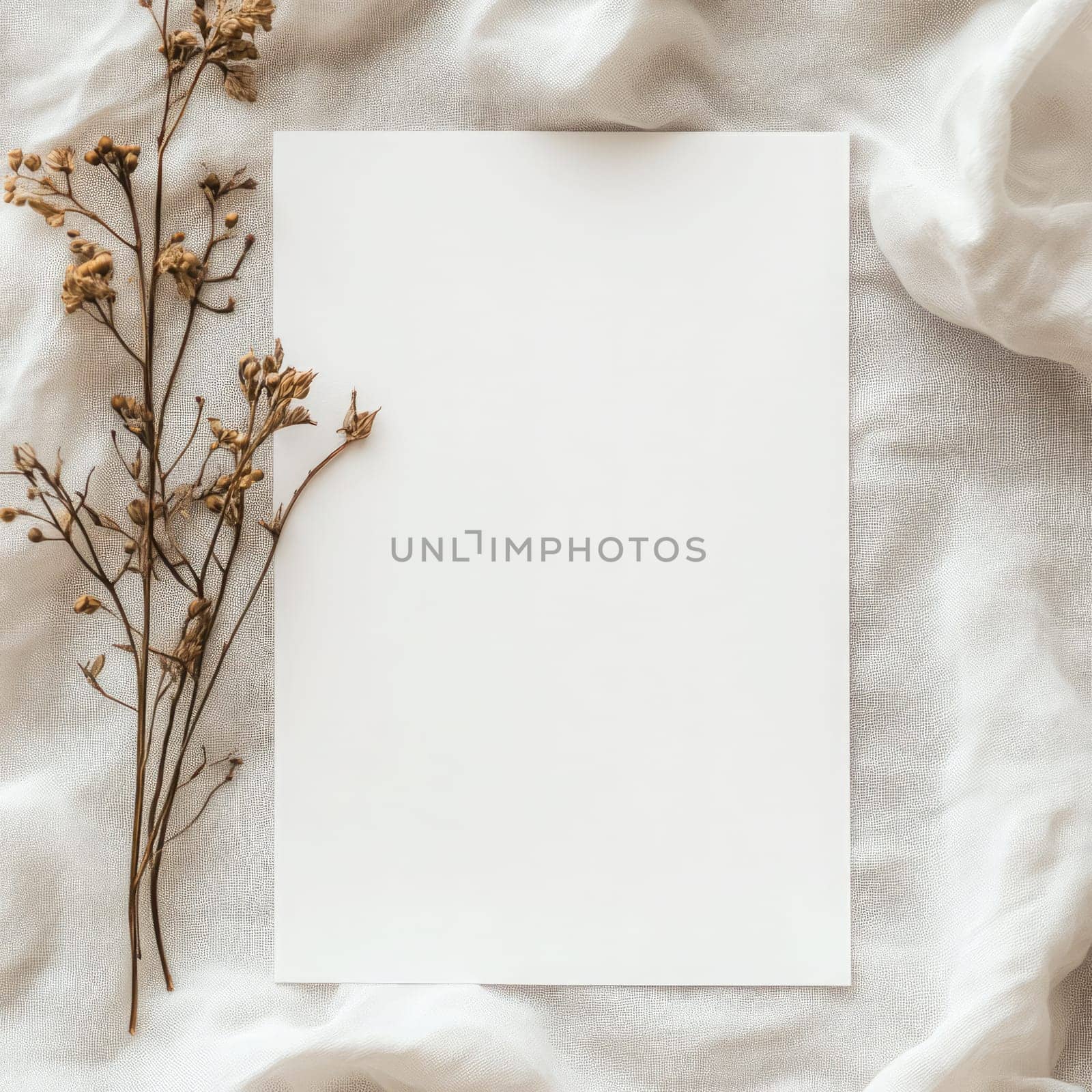 A piece of blank paper lies on a textured fabric backdrop surrounded by delicate dried flowers, creating an inviting space for writing or artistic projects.