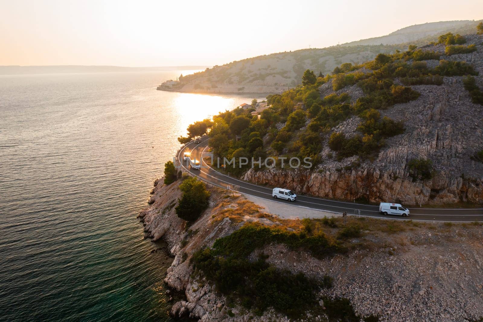 Scenic coastal road travels along the waterfront at sunset in a beautiful mountainous region.