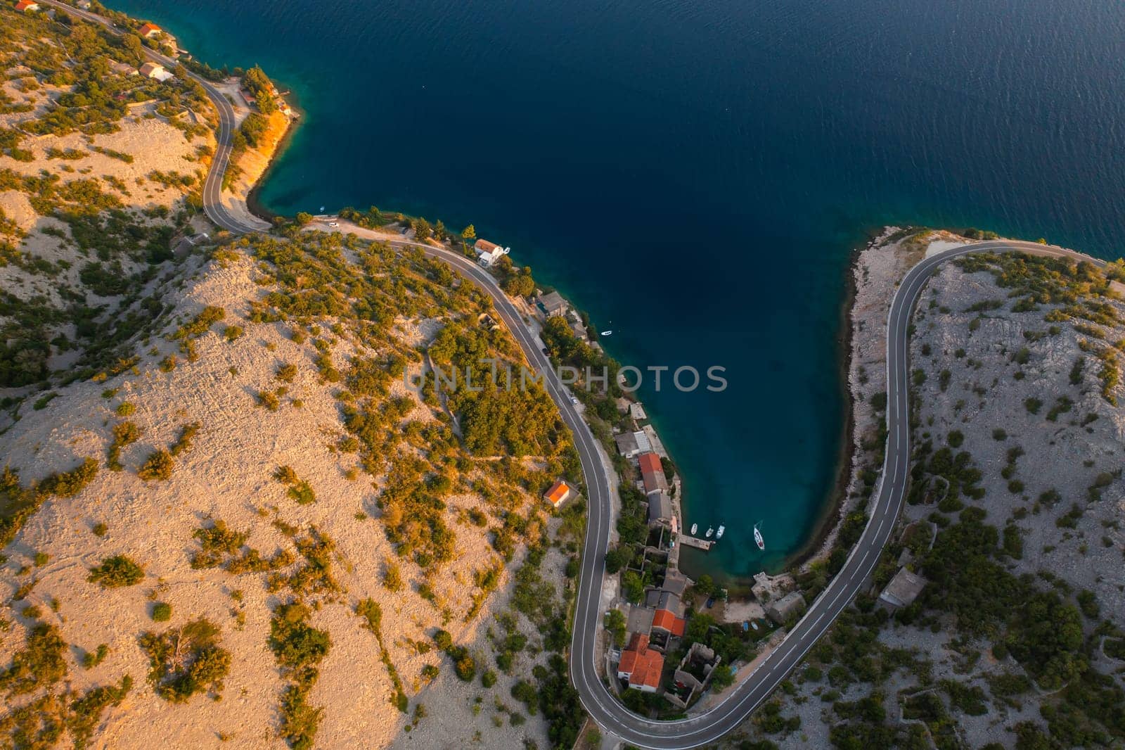 Aerial view of a winding coastal road near the tranquil blue waters of a secluded cove.
