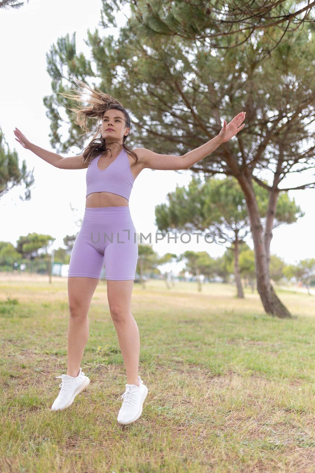 A young woman in a purple sports outfit jumps in the air, surrounded by green trees.