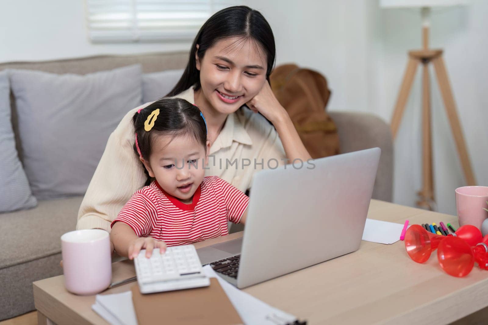 Curious toddler exploring the laptop with the guidance of her mother, representing shared digital learning experiences at home.