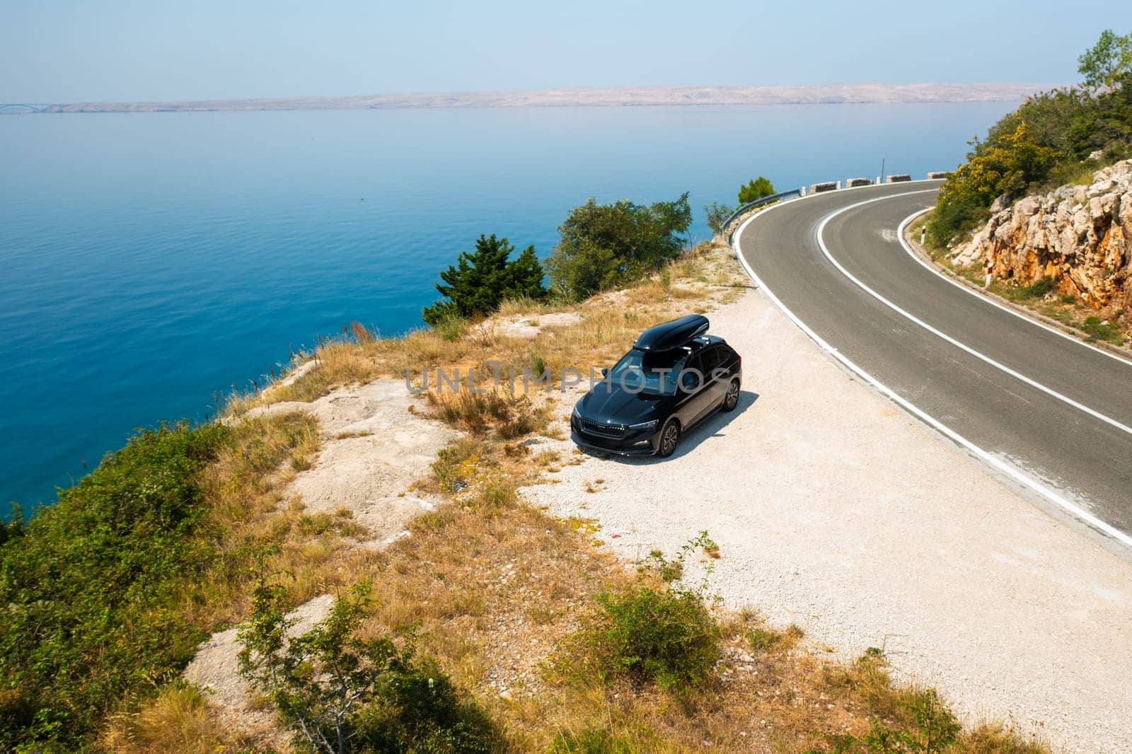 Car with a roof box stands on the side of a cliff and beautiful rocks in the background.