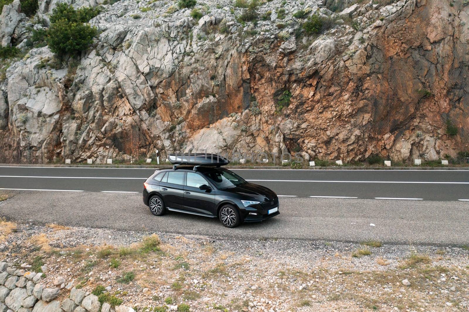 A black car parked on the roadside beside rocky cliffs during daytime travel.
