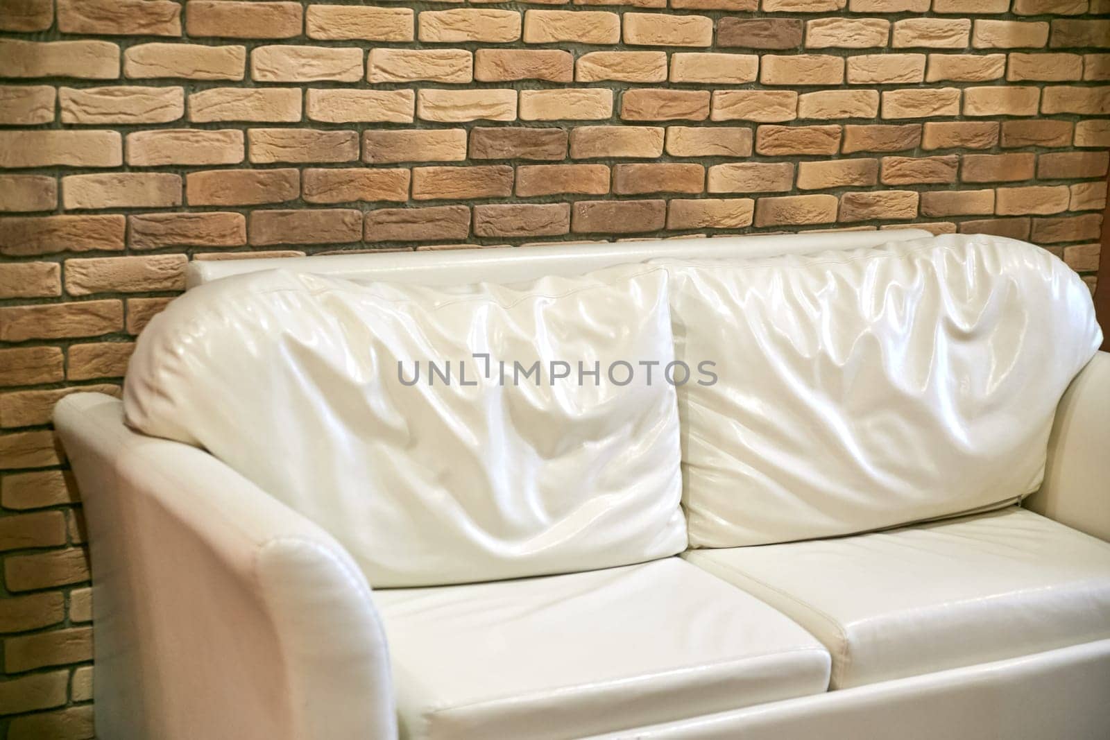 There is a stylish white couch placed in front of a rustic brick wall, creating an appealing contrast between modern furniture and traditional building materials