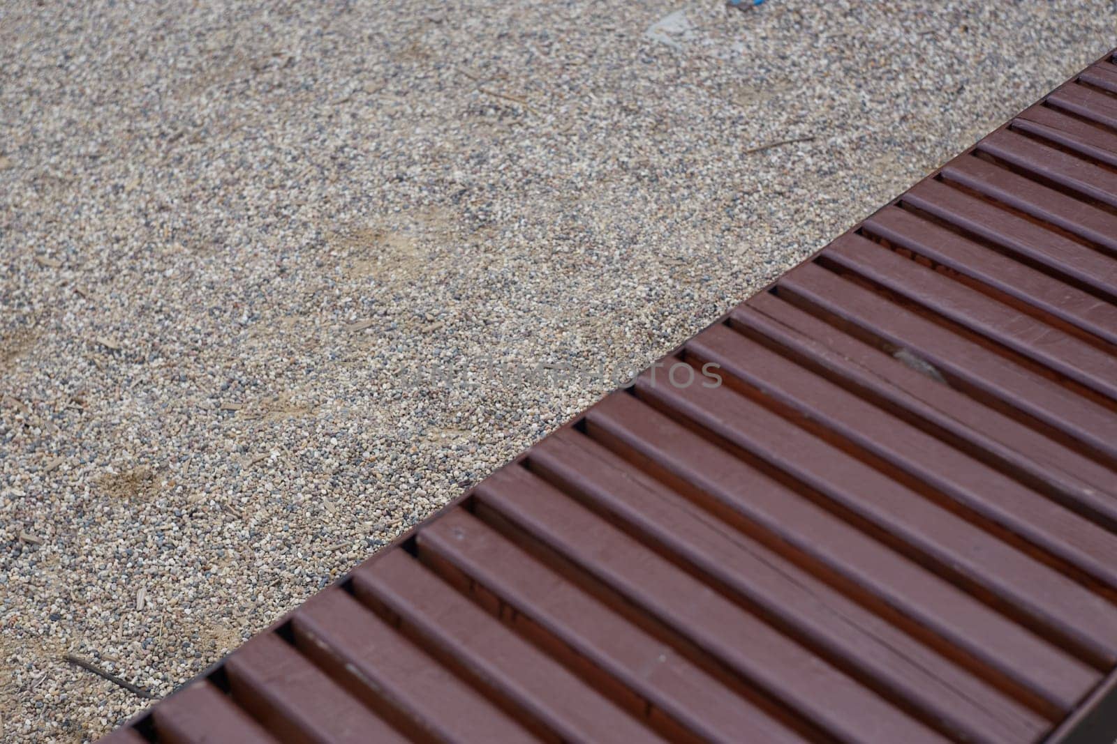 The playground is covered with gravel and a wooden brown bench