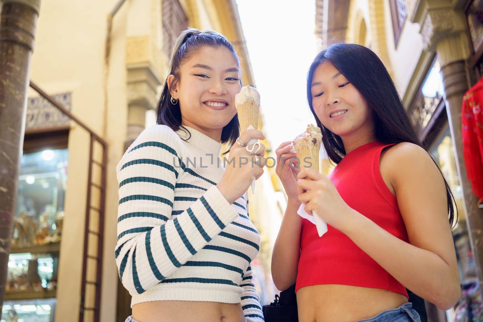 Two young Chinese girls eating an ice cream cone in the typical streets of Granada, Spain. Concept of Asian people traveling in Europe.