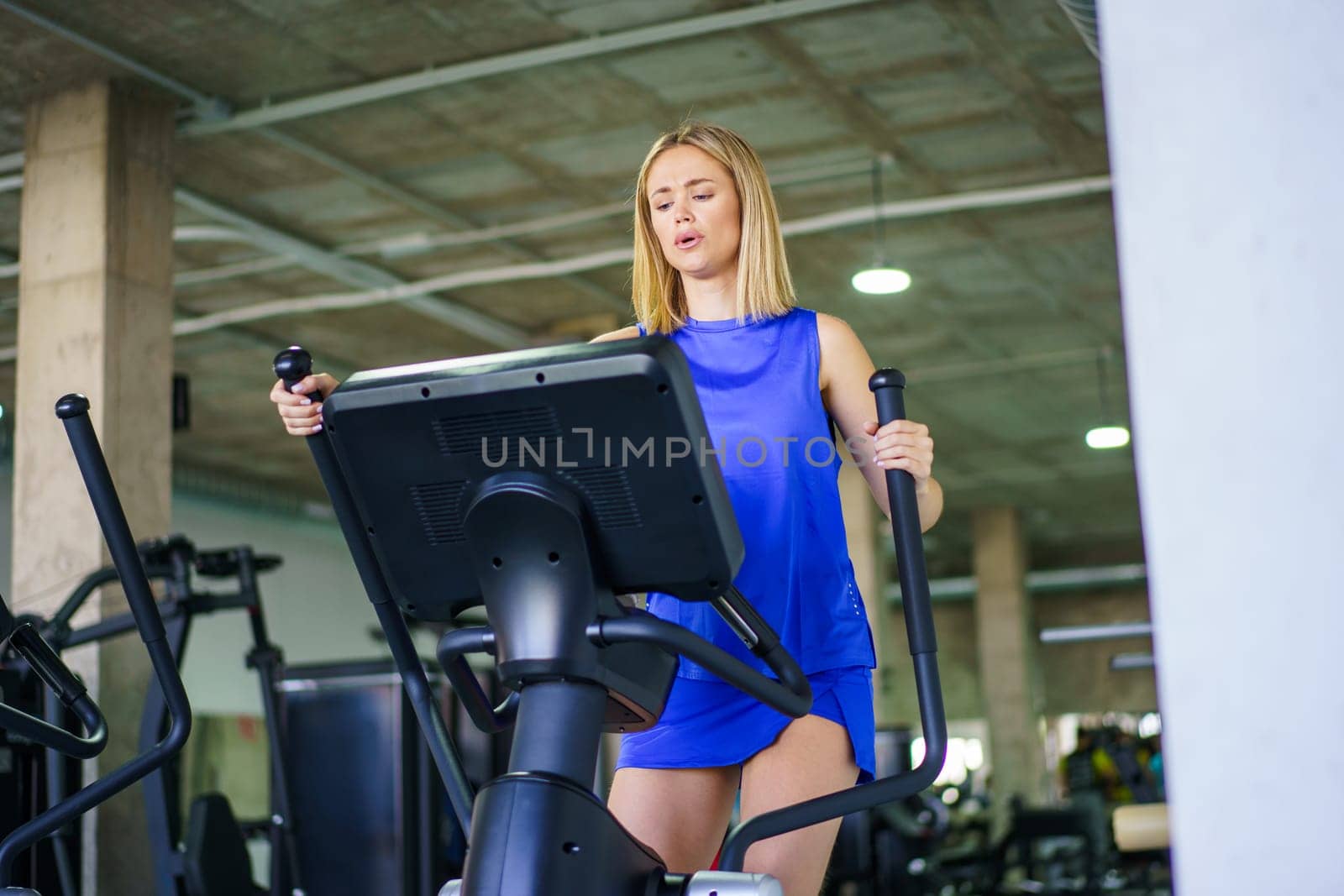 Low angle view horizontal photo with copy space of a blonde young caucasian woman walking exercising in elliptical machine in the gym
