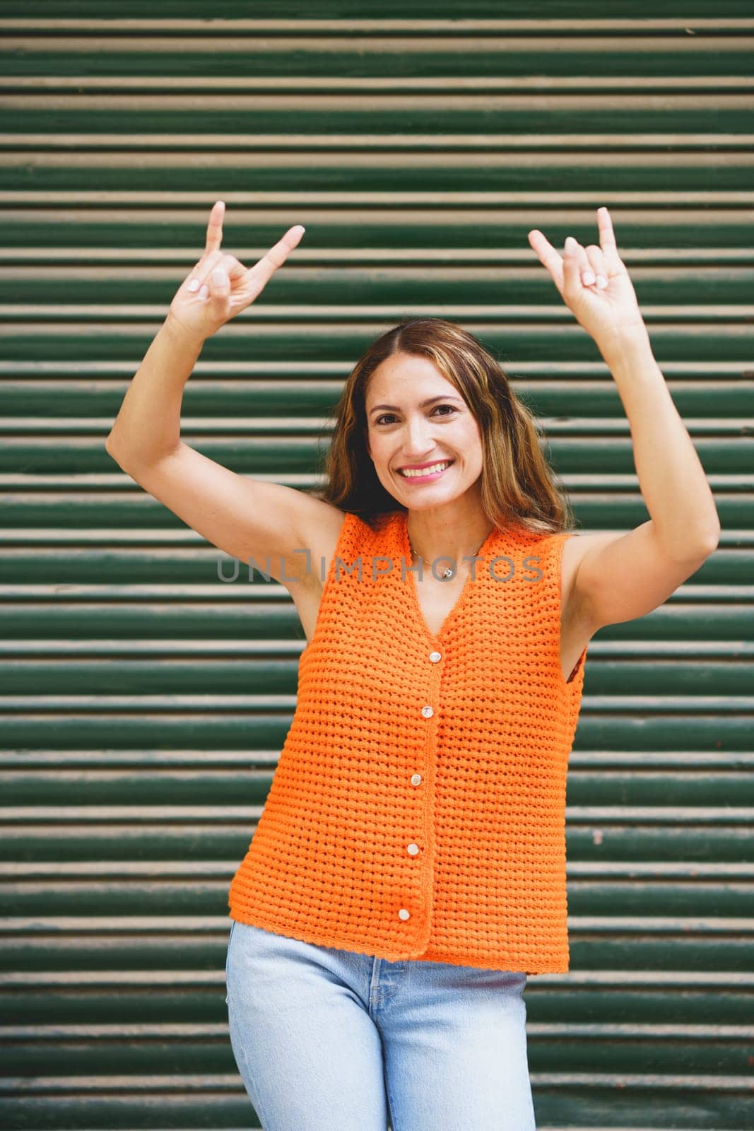 Vertical photo of a latin woman smiling doing the heavy metal horns hand sign