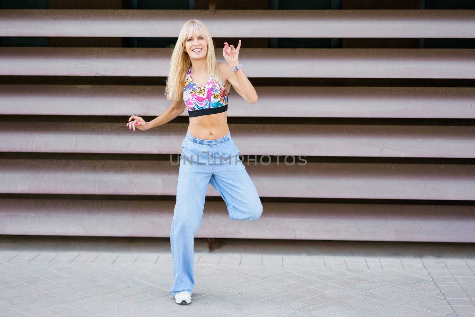Smiling blonde young woman dancing freestyle modern music in the street