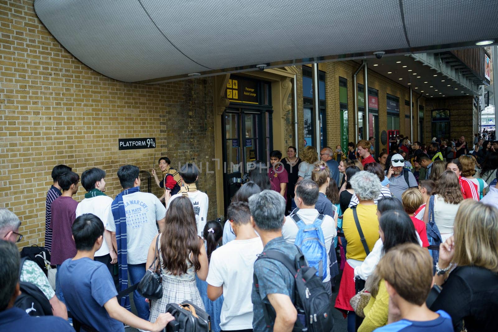 London, UK, july 20th 2024. Japanese young people pretending to hold a wand as people queue for a photo with the Harry Potter trolley on the imaginary platform 9 3-4 at King's Cross station.