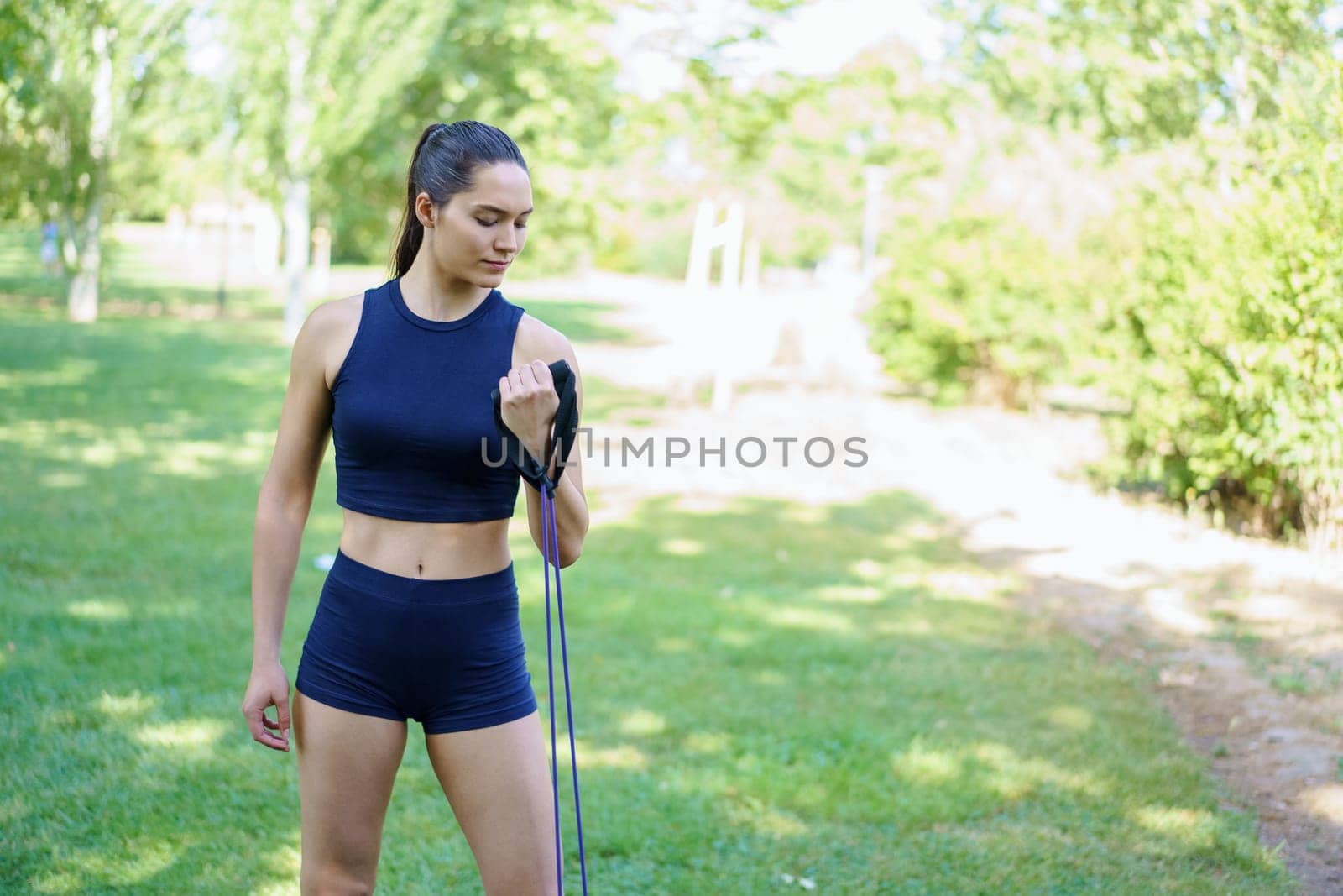 In the sunny park, a woman in activewear is using a resistance band for strength and conditioning exercises. She is effectively toning her body during this outdoor training session