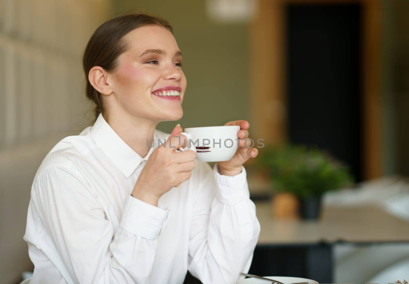 Smiling businesswoman enjoying a delicious aromatic coffee in a cafeteria sitting alone holding the mug