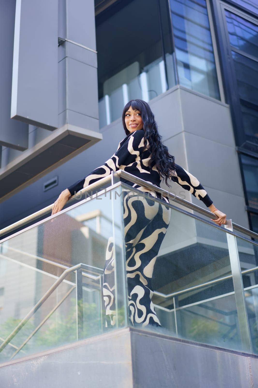Vertical low angle view of a dancer posing leaning on a rail in the city