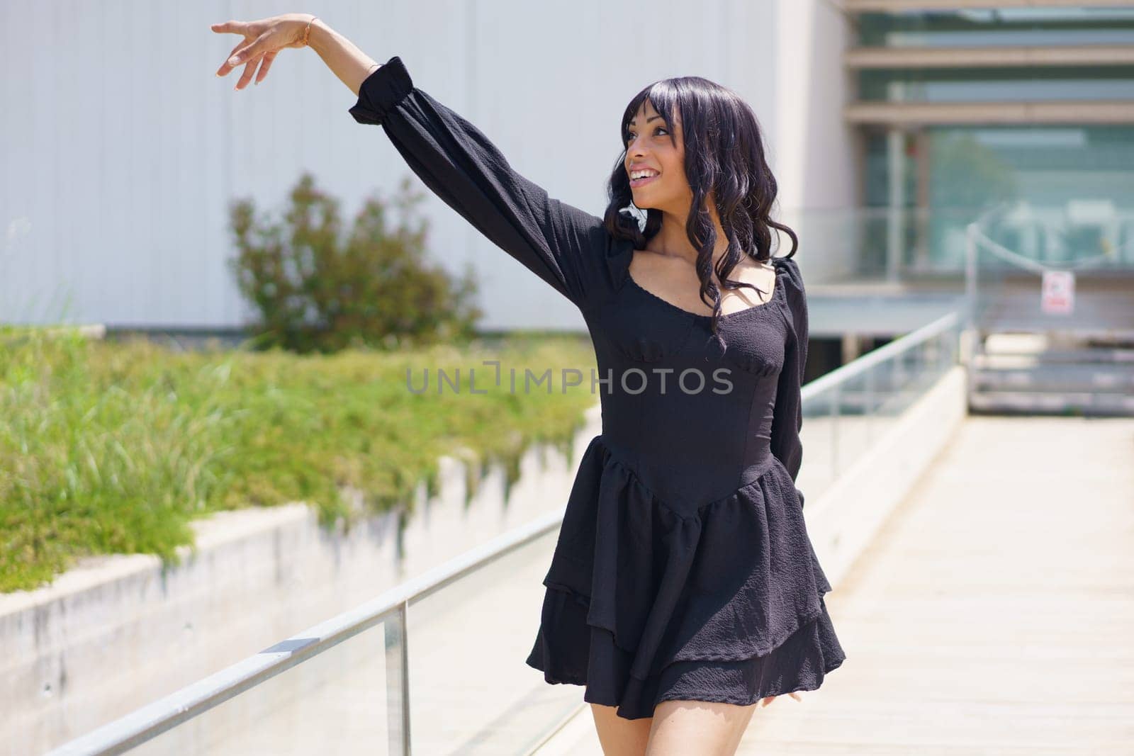 Vital woman raising hand while dancing under the sun in the city