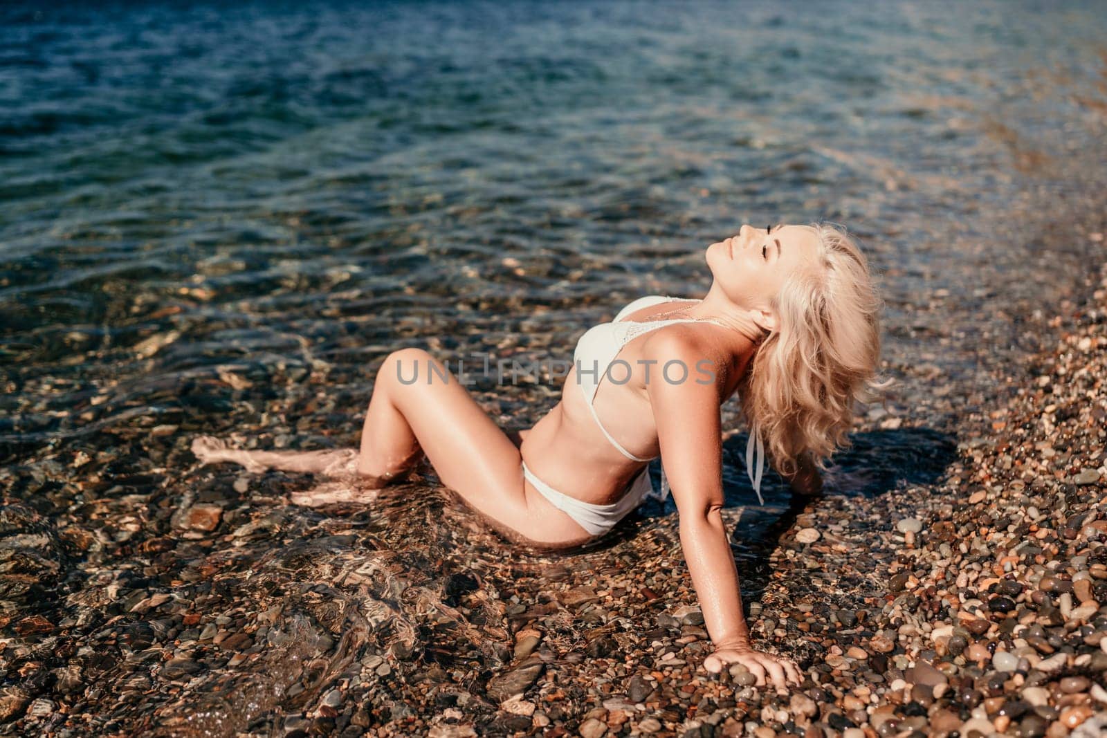 A woman in a bikini is laying on the beach in the water. She is smiling and enjoying the sun