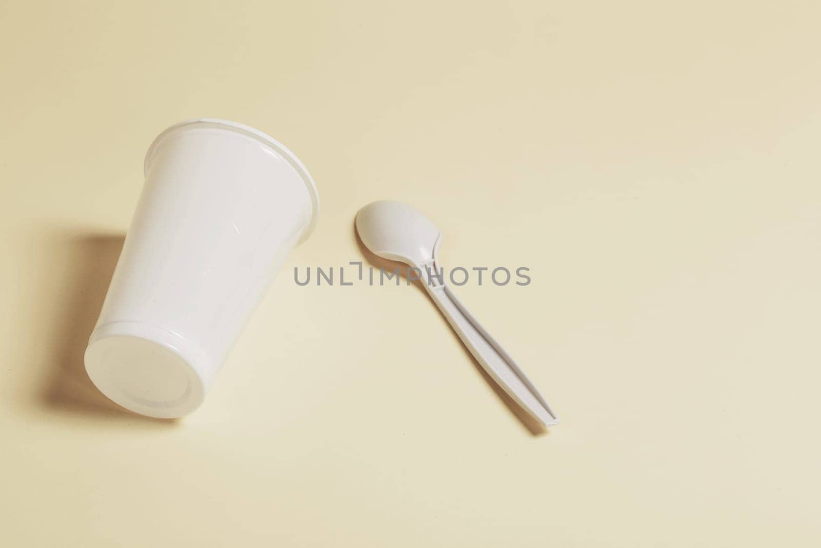 White plastic glass and spoon on a paper background.