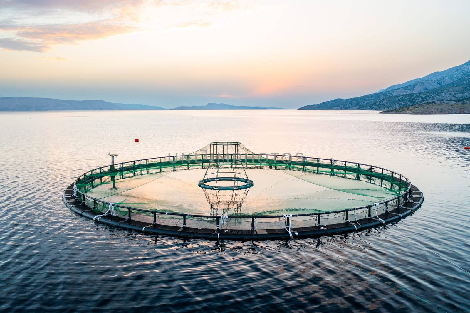 Fish farm setup on calm waters at sunset in a rural location.