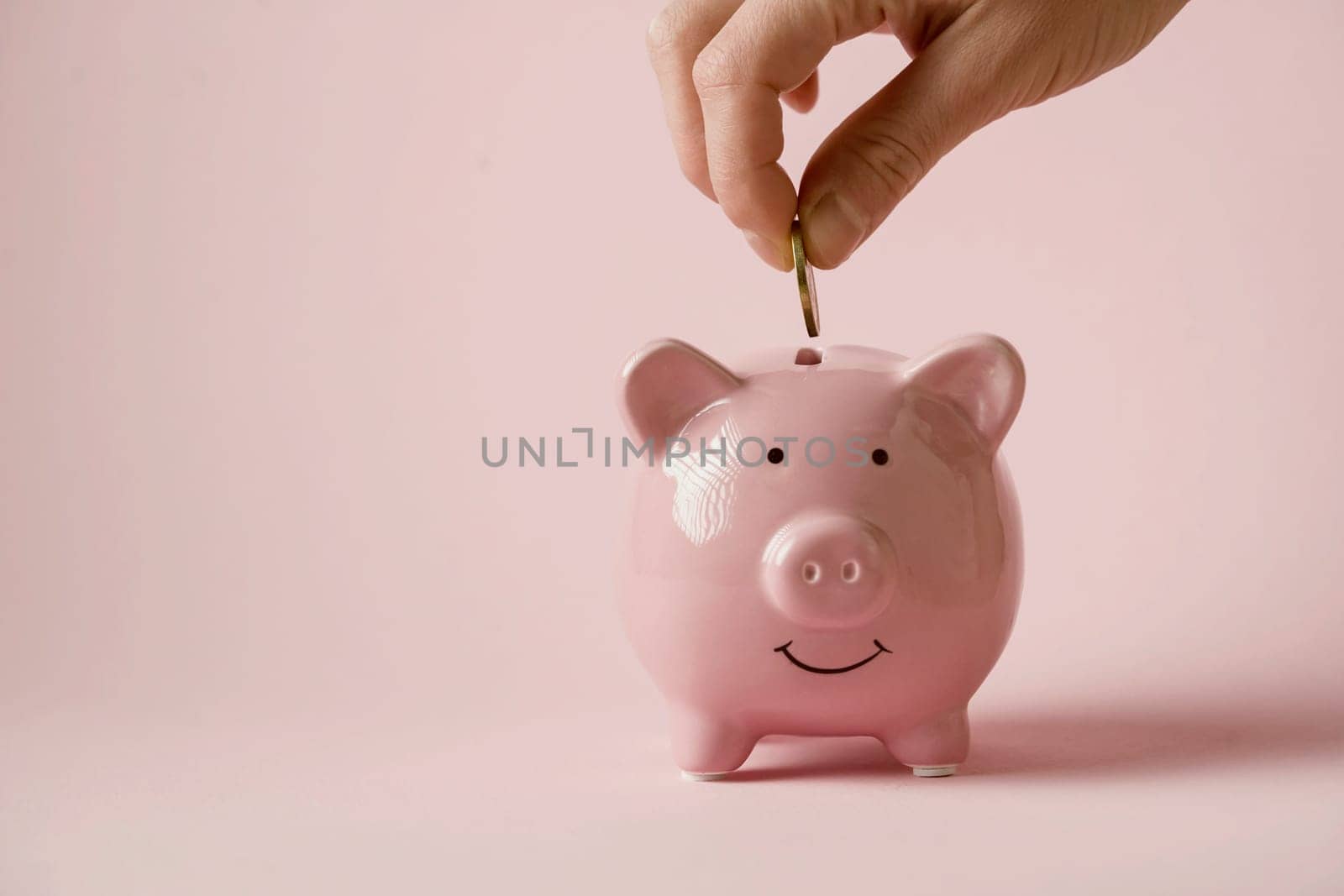 The hand holds a coin and puts it in a piggy bank to preserve wealth, savings and financial success.