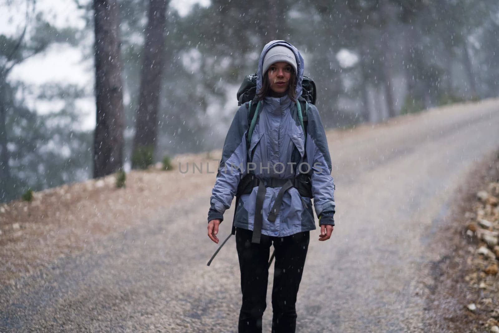 A young happy girl with hiking equipment and a backpack walks along the paths, in the mountains under the snowfall. The woman leads an active lifestyle and travels through the wilderness.