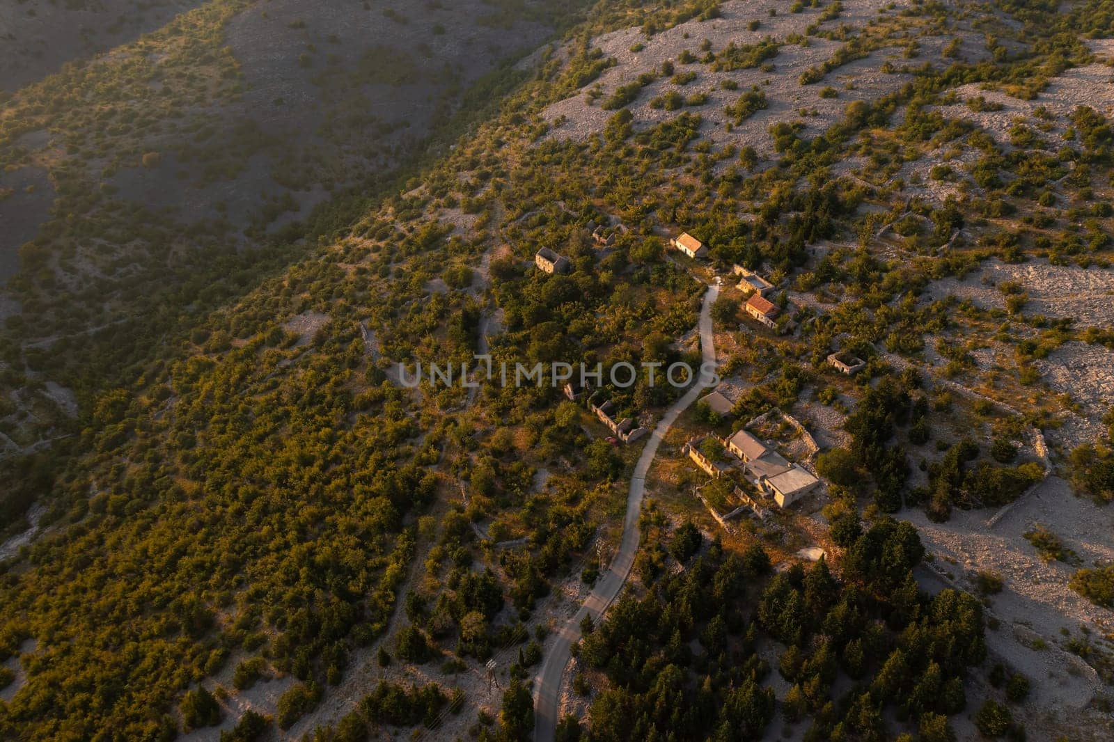 Aerial view of a serene village surrounded by lush greenery during sunset in a mountainous area.