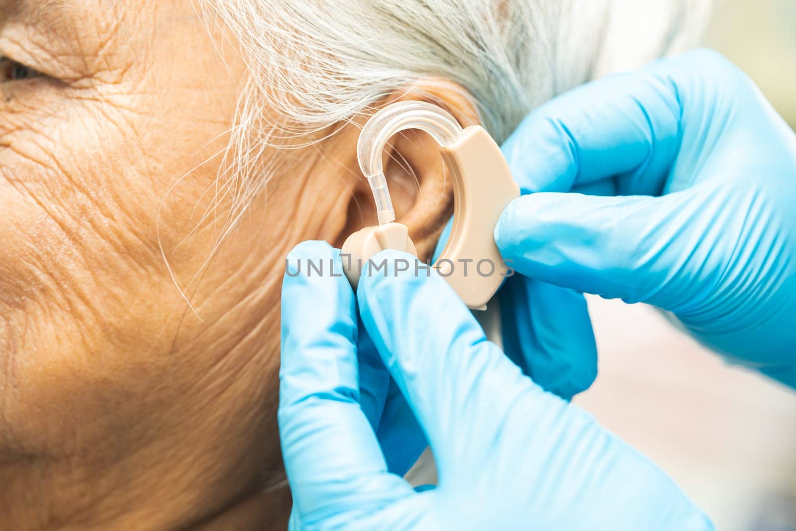 Asian senior woman patient wearing a hearing aid for treating hearing loss problem. by pamai