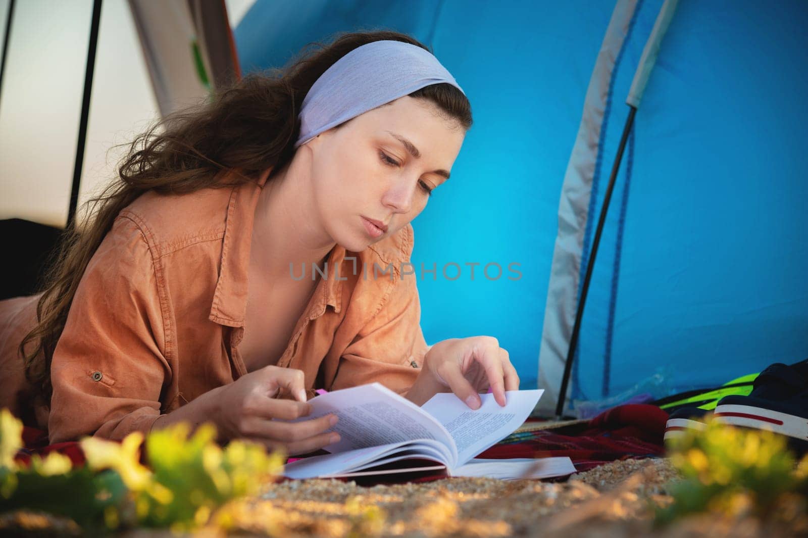 Caucasian woman thoughtfully reading a book on a beautiful beach. Beautiful girl in casual clothes looks at a book while lying on the sand, bottom view from ground level by yanik88