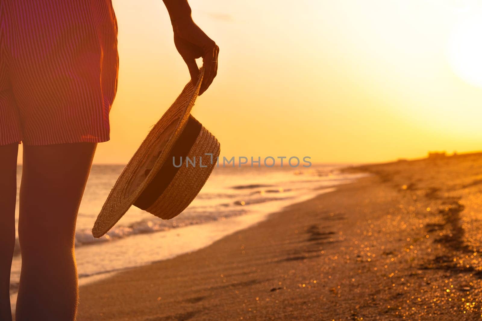 Detail of a straw hat held by a woman. Close-up of a straw hat in a woman's hand against the background of the sea or ocean. Vacation concept. Sea resort, travel.
