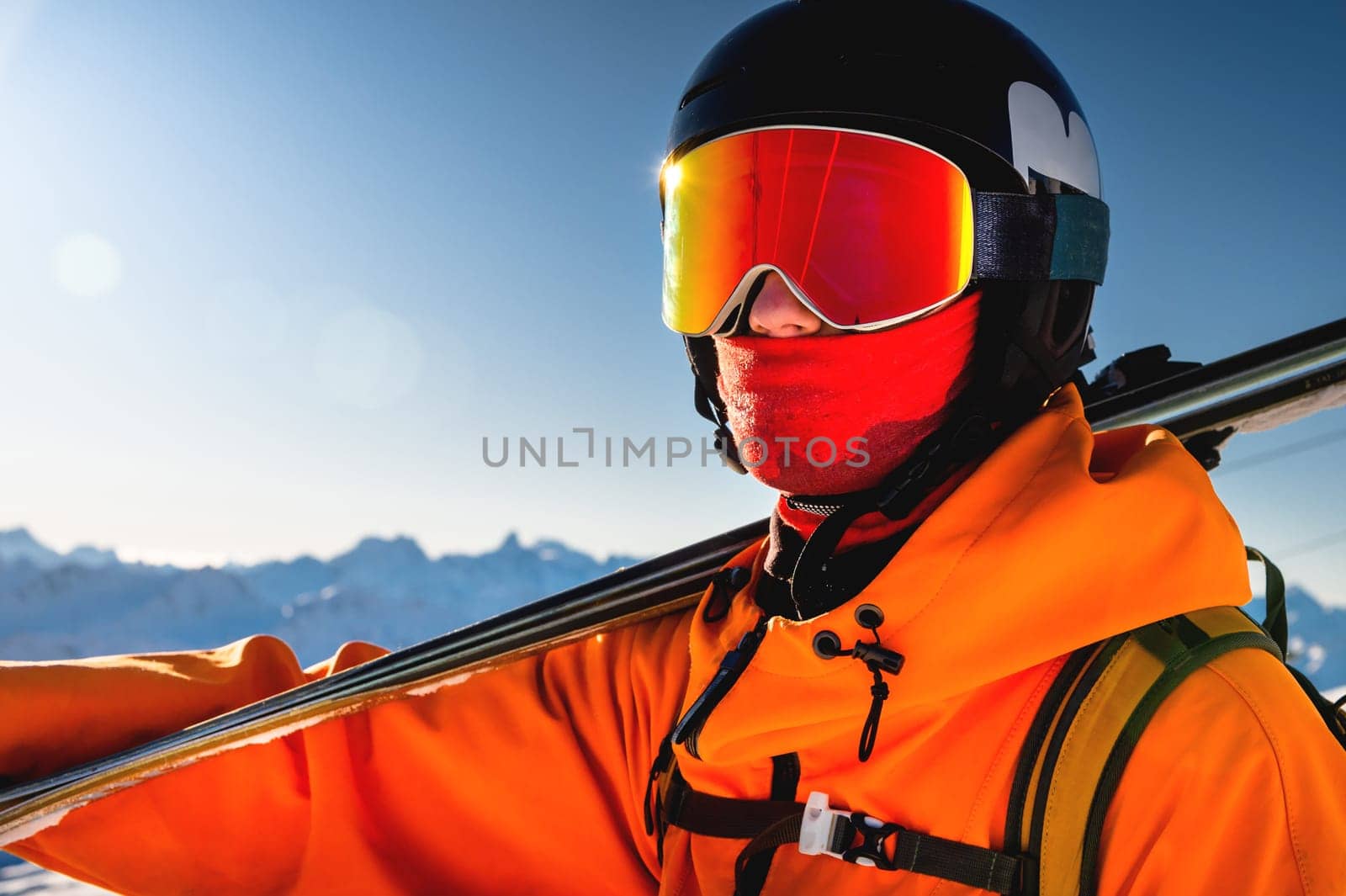 Portrait of a skier with skis on his shoulder. Guy on a background of a mountain range on a sunny winter day, sunlight, outdoor recreation, skiing, sports concept.